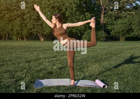 Eine junge Frau praktiziert Yoga in einem Stadtpark, während sie in einer Kriegerpose steht. Stockfoto