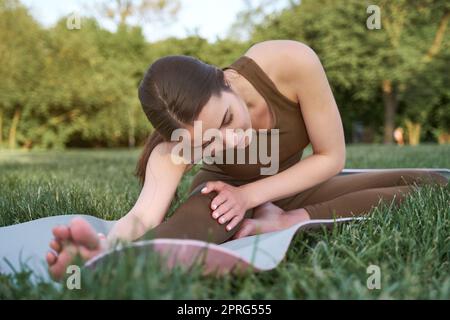 Sportlerin macht Yoga-Bewegung und entspannen mit Sportbekleidung im grünen Park im Sommer, gesundes Lifestyle-Konzept Stockfoto