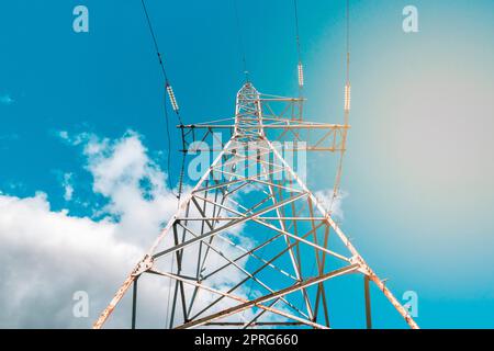 Hochspannungsturm mit Stromübertragungsleitungen gegen blauen Himmel Stockfoto