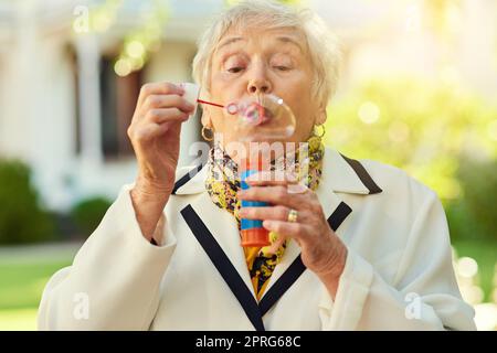 Sie sind nur so alt, wie Sie sich fühlen. Eine lebenslustige ältere Frau bläst an einem sonnigen Tag draußen Blasen. Stockfoto