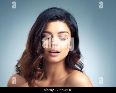 Feminin und oh so fein. Studioaufnahme einer schönen jungen Frau, die vor einem grauen Hintergrund posiert. Stockfoto