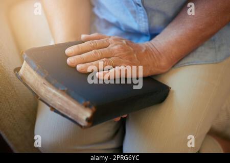 Das Wort birgt jede Hoffnung und jeden Trost, den Sie suchen. Nahaufnahme einer älteren Frau, die zu Hause eine Bibel hält. Stockfoto