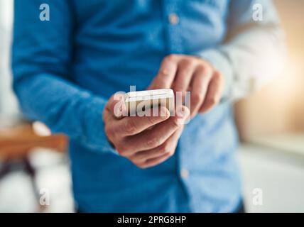 Geschäftsabläufe erledigen. Nahaufnahme eines Geschäftsmannes, der in einem Büro auf einem Mobiltelefon SMS schreibt. Stockfoto