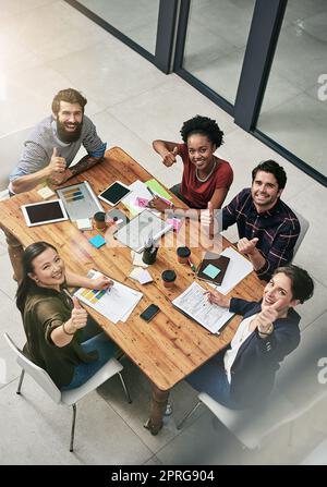 Wir gewinnen, wenn wir als Einheit arbeiten. Hochwinkelporträt einer Gruppe von Kollegen, die während einer Besprechung in einem modernen Büro den Daumen nach oben geben. Stockfoto