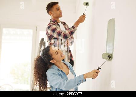 Gemälde, Liebe und Renovierung mit einem Paar, das Heimwerker ist, in einem Raum für Renovierung und Renovierung seines Hauses. Junger Mann und Frau, die mit grüner Farbe an einer Wand arbeiten, um ihr Haus zu renovieren Stockfoto