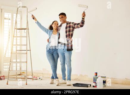 Porträt eines glücklichen Paares, das das neue Wohnzimmer in einem Haus oder einer Wohnung streicht. Mann und Frau mit Pinsel zur Dekoration einer Wandfarbe und Renovierung der Inneneinrichtung mit Lächeln oder Glück zusammen Stockfoto