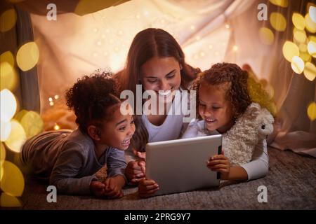 Mutter und Kinder streamen live Filme auf einem Tablet oder einer digitalen Kinder-App in einem Zelt, Camping bei Nacht und Bokeh-Lichter. Care, Love mom liest eBook für glückliche Mädchen oder Online-Spiele mit Heim-WLAN im Dunkeln Stockfoto