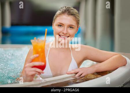 Lassen Sie uns auf einen Tag voller Luxus anstoßen. Porträt einer jungen Frau, die einen Cocktail im Pool in einem Spa trinkt. Stockfoto