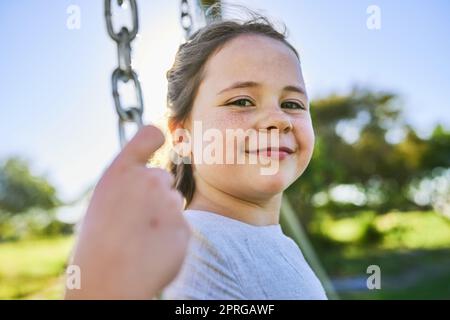 Schwingt im Sonnenschein. Porträt eines niedlichen kleinen Mädchens, das auf einer Schaukel in einem Park sitzt. Stockfoto