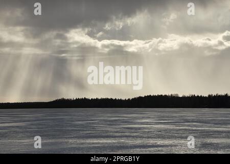 Am Horizont regnet es über dem gefrorenen See in Finnland Stockfoto