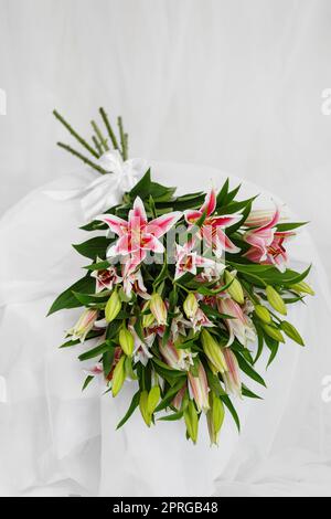 Schöner großer Strauß rosa Lilien liegt auf einem weißen Stoffhintergrund Stockfoto