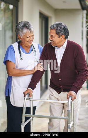 Die richtigen Schritte zu einem gesünderen Wohlbefinden. Eine Krankenschwester geht mit ihrem älteren Patienten und seinem Spaziergänger draußen spazieren. Stockfoto