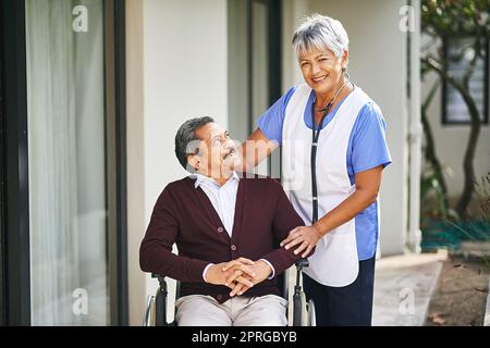 Freundlichkeit und Mitgefühl gehen einen langen Weg. Ein älterer Mann im Rollstuhl wird von einer Krankenschwester in einem Altersheim betreut. Stockfoto