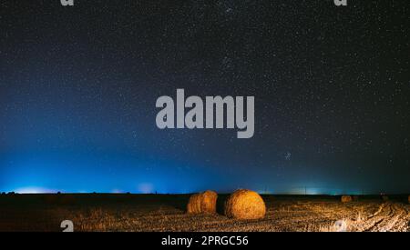 Nacht Sternenhimmel Über Haystacks Im Sommer Landwirtschaftlichen Feld. Nachtsterne Über Der Ländlichen Landschaft Mit Heuballen Nach Der Ernte. Landwirtschaftliches Panorama Stockfoto