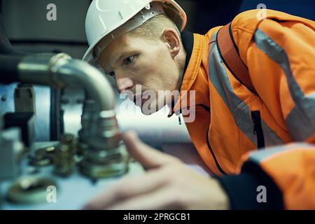 Kleine Probleme lösen, bevor sie zu großen Problemen werden. Aufnahme eines jungen Ingenieurs, der mit komplizierten Maschinen arbeitet, während er Sicherheitsausrüstung trägt. Stockfoto