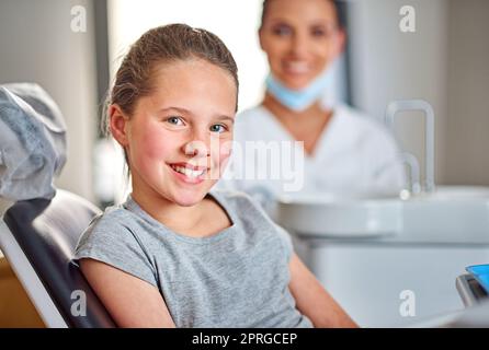 Shes in für eine Routineprüfung. Aufnahme eines jungen Mädchens, das auf einem Zahnarztstuhl sitzt und im Hintergrund ihren Zahnarzt hat. Stockfoto