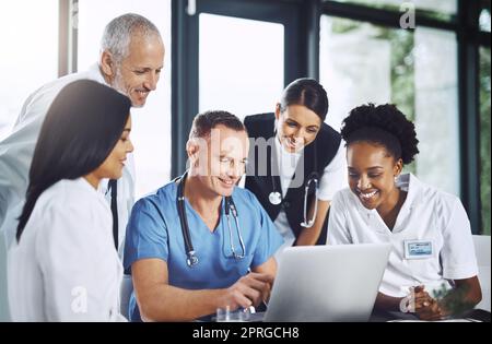 Es ist ein Treffen von medizinischen Köpfen. Eine Gruppe von medizinischen Fachleuten um einen Laptop im Sitzungssaal versammelt. Stockfoto