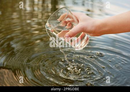 Seid wasserklug. Wasser wird aus einem Glas in einen Teich gegossen. Stockfoto