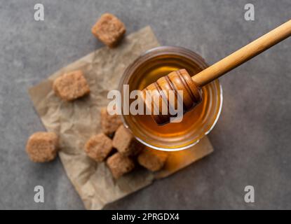 Brauner Zucker mit Honig und Holzhonig-Dipper auf steinernem Hintergrund. Bild von Schönheit. Blick von oben. Stockfoto