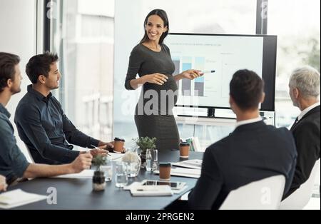 Eine schwanger Geschäftsfrau, die eine Präsentation auf einem Monitor vor Kollegen in einem Sitzungssaal gibt. Stockfoto