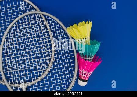 Bunt gefiederte Bälle in Blau, Gelb und Pink und Badminton Schläger auf blauem Hintergrund in der Nähe zu sehen. Stockfoto