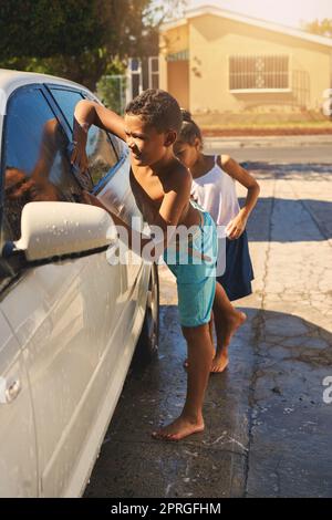 Ein kleiner Junge und ein Mädchen waschen draußen gemeinsam ein Auto. Stockfoto