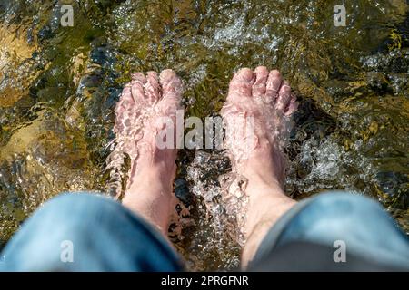 Fließendes Wasser zwischen Steinen schlägt die Füße eines Mannes in der Sonne Stockfoto