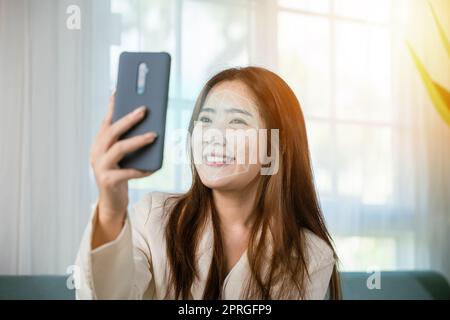 Asiatische Frauen verwenden Smartphone für die Zugangskontrolle Gesichtserkennung bei der privaten Identifikation auf dem Sofa Wohnzimmer zu Hause Stockfoto