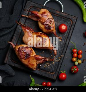 Das Frittieren der Wachtelkadaver liegt auf einem Holzbrett mit Gemüse Stockfoto