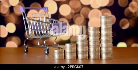 Leer Warenkorb und Geld Stapeln in Wachstum graph auf dem Hintergrund der farbigen Bokeh christmas lights. Shopping Zeitraum Konzept Stockfoto