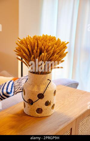 Ein Blatt oder ein Strauß getrockneter Weizenstiele steht in einer Vase auf einem Holztisch vor einem hellen Vorhanghintergrund. Modernes Frühlingsdesign. Trockene Blumen. Stockfoto