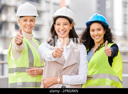 Alle Standards wurden erfüllt. Gekürztes Porträt von drei attraktiven Ingenieurinnen, die auf einer Baustelle draußen mit erhobenem Daumen stehen Stockfoto