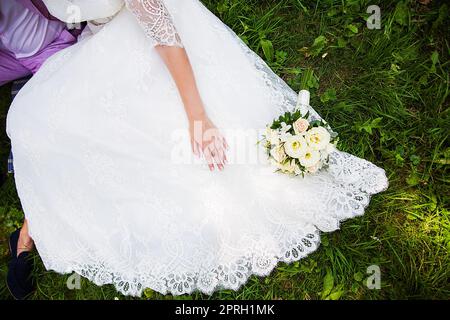 Braut und Bräutigam sitzen auf dem Gras mit schönen Blumenstrauß Stockfoto