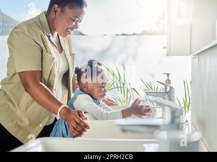 Der beste Weg, Kindern Hygiene beizubringen, ist früh anzufangen. Eine Mutter, die ihrer Tochter beim Händewaschen zuhause im Badezimmer hilft Stockfoto