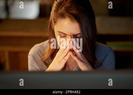 Shes, die eine harte Zeit haben. Eine attraktive junge Geschäftsfrau, die gestresst aussieht, während sie spät im Büro arbeitet. Stockfoto