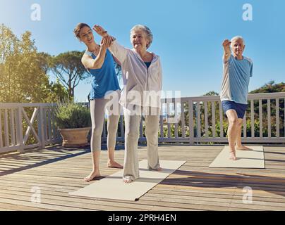 Gesund bleiben im Ruhestand. Ein Seniorenpaar macht Yoga zusammen mit einem Lehrer auf ihrer Terrasse draußen. Stockfoto