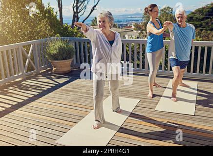 Yoga ist Bewegung für Körper und Geist. Ein Seniorenpaar macht zusammen mit einem Lehrer auf der Terrasse Yoga. Stockfoto