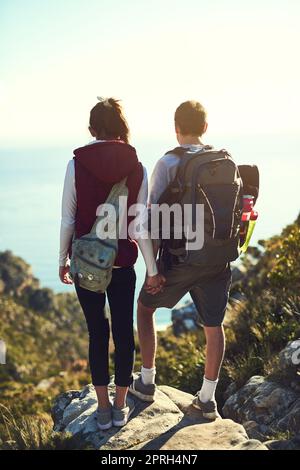 Es gibt keine Abkürzungen zu allem, was sich lohnt. Rückansicht eines jungen Paares, das die Aussicht von der Spitze eines Berges bewundert. Stockfoto