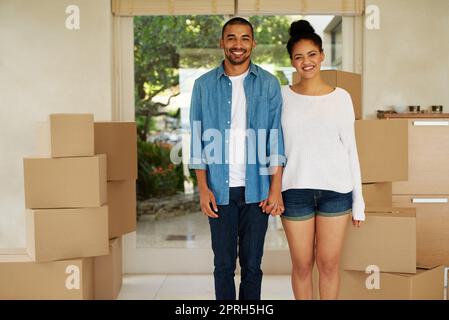 Unser neues Abenteuer beginnt hier. Porträt eines glücklichen jungen Paares, das in ihrem neuen Zuhause zwischen Kartons steht. Stockfoto