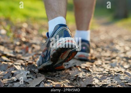 Ein Fuß vor dem anderen. Rückansicht eines nicht erkennbaren männlichen Athleten, der durch den Wald wandert. Stockfoto