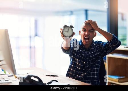 Es gibt einfach zu viel, um mit zu wenig Zeit zu tun. Porträt eines jungen Designers, der gestresst aussieht und einen Wecker hält. Stockfoto