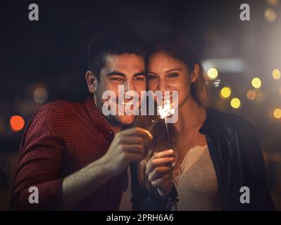 Finden Sie eine Liebe, die Sie funkeln lässt. Ein glückliches junges Paar feiert mit Wunderkerzen draußen in der Nacht. Stockfoto