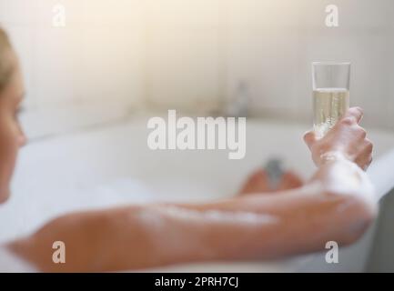 Eine junge Frau, die sich bei einem Glas Wein in der Badewanne entspannt. Stockfoto