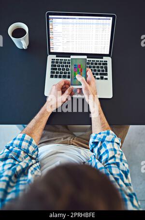 Mit Hilfe von Technologie näher an die Geschäftsziele heranzukommen. High-Angle-Aufnahme eines jungen Designers, der in einem modernen Büro ein Mobiltelefon verwendet. Stockfoto