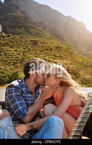 Die Liebe ist ein großes Abenteuer. Ein junges Paar teilt sich einen Kuss ganz auf der Rückseite eines Pickup-Truck. Stockfoto