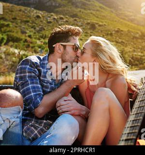 Erleben Sie eine ganz neue Seite der Liebe auf ihrer Roadtrip. Ein junges Paar teilen sich einen Kuss ganz auf der Rückseite eines Pickup-Truck. Stockfoto