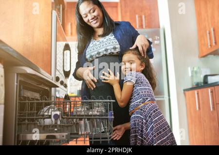 Bald wird Mama einen weiteren kleinen Engel haben. Porträt einer Tochter, die ihre Schwangeren in der Küche umarmt. Stockfoto