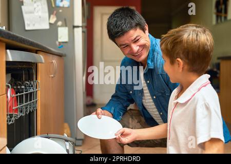 Ein Vater und ein Sohn sind an einer Spülmaschine beschäftigt. Stockfoto