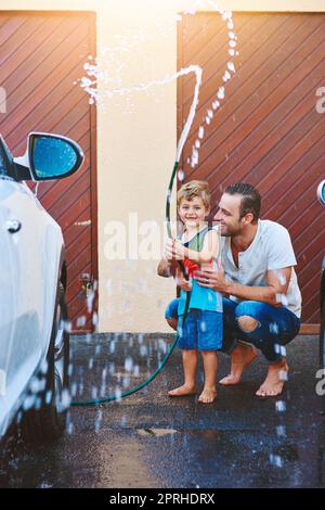 Es gibt Spaß zu haben, während der Arbeit zu tun. Die ganze Aufnahme eines Vaters und eines Sohnes, die mit einer Schlauchleitung spielen, während sie ein Auto gemeinsam waschen. Stockfoto