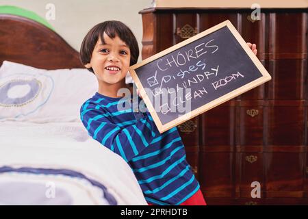 Fast fertig mit den Aufgaben. Porträt eines Jungen mit einer Tafel und aufgeschriebenen Aufgaben. Stockfoto